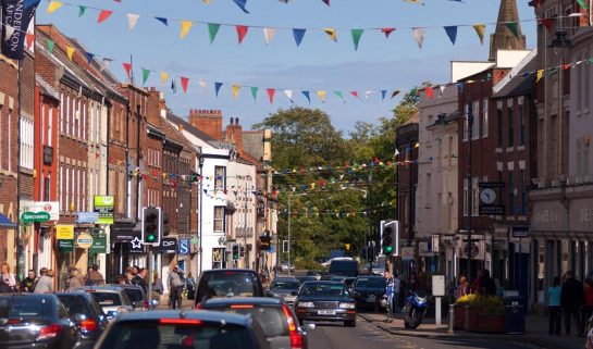 Image shows Morpeth's High Street on a sunny day with bunting flying overhead across the road.